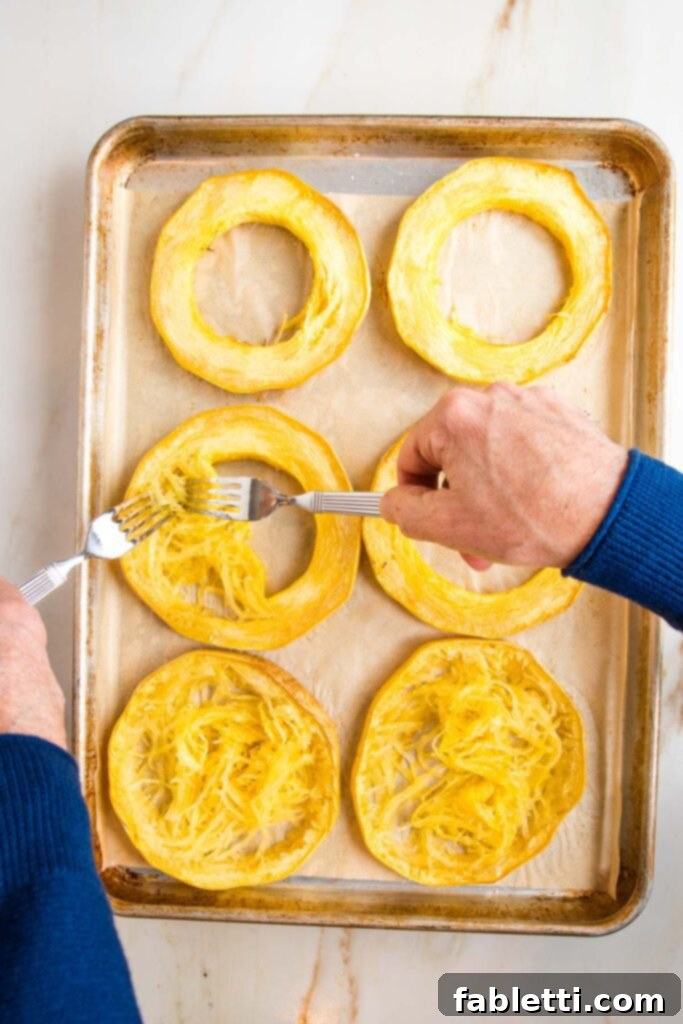Hearty Vegan Bolognese over Squash Strands 18 A large rimmed baking sheet holding roasted spaghetti squash rings. Two forks are actively pulling the spaghetti-like strands from the squash skins.