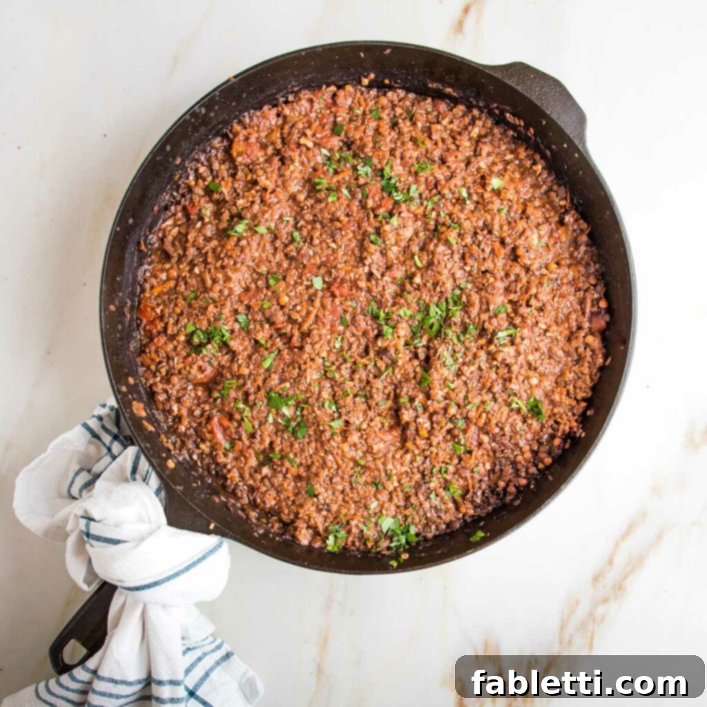 Hearty Vegan Bolognese over Squash Strands 19 A rich, chunky vegan bolognese sauce simmering in a cast iron skillet, garnished with a sprinkle of fresh parsley.
