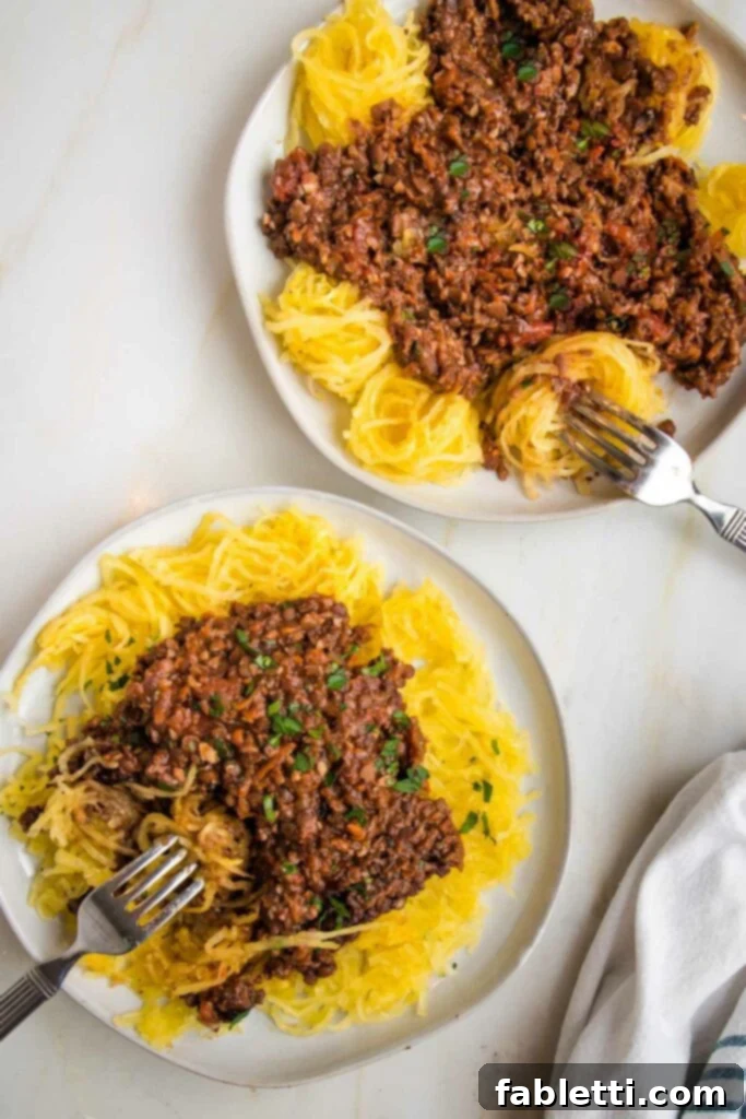 Hearty Vegan Bolognese over Squash Strands 24 Two white rimmed plates, each generously filled with perfectly cooked spaghetti squash and topped with the rich, chunky vegan bolognese sauce.