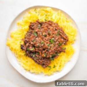 Hearty Vegan Bolognese over Squash Strands 25 A white rimmed plate filled with spaghetti squash and covered with a generous serving of red lentil vegan bolognese sauce.