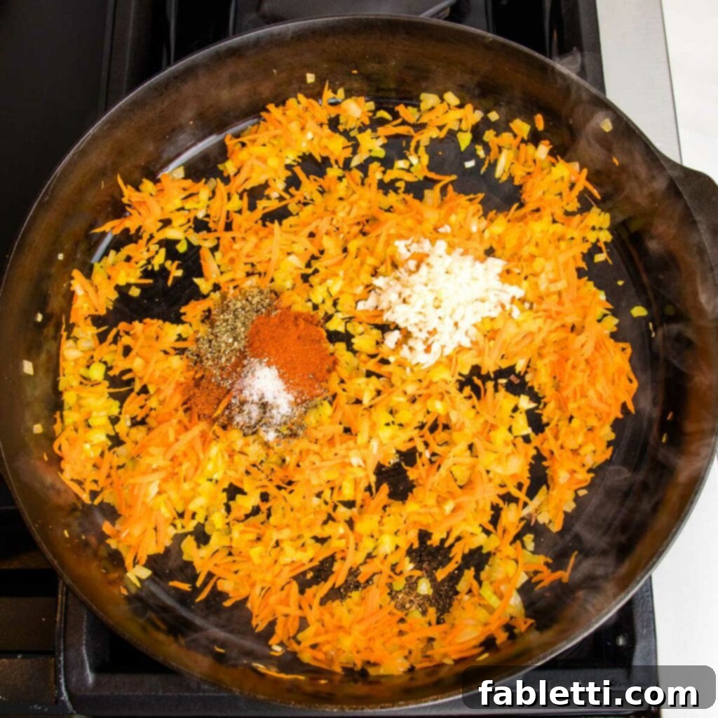 Hearty Vegan Bolognese over Squash Strands 9 Sautéed carrots, onions, and celery in a cast iron skillet, with spices and minced garlic freshly added and ready to be stirred in.