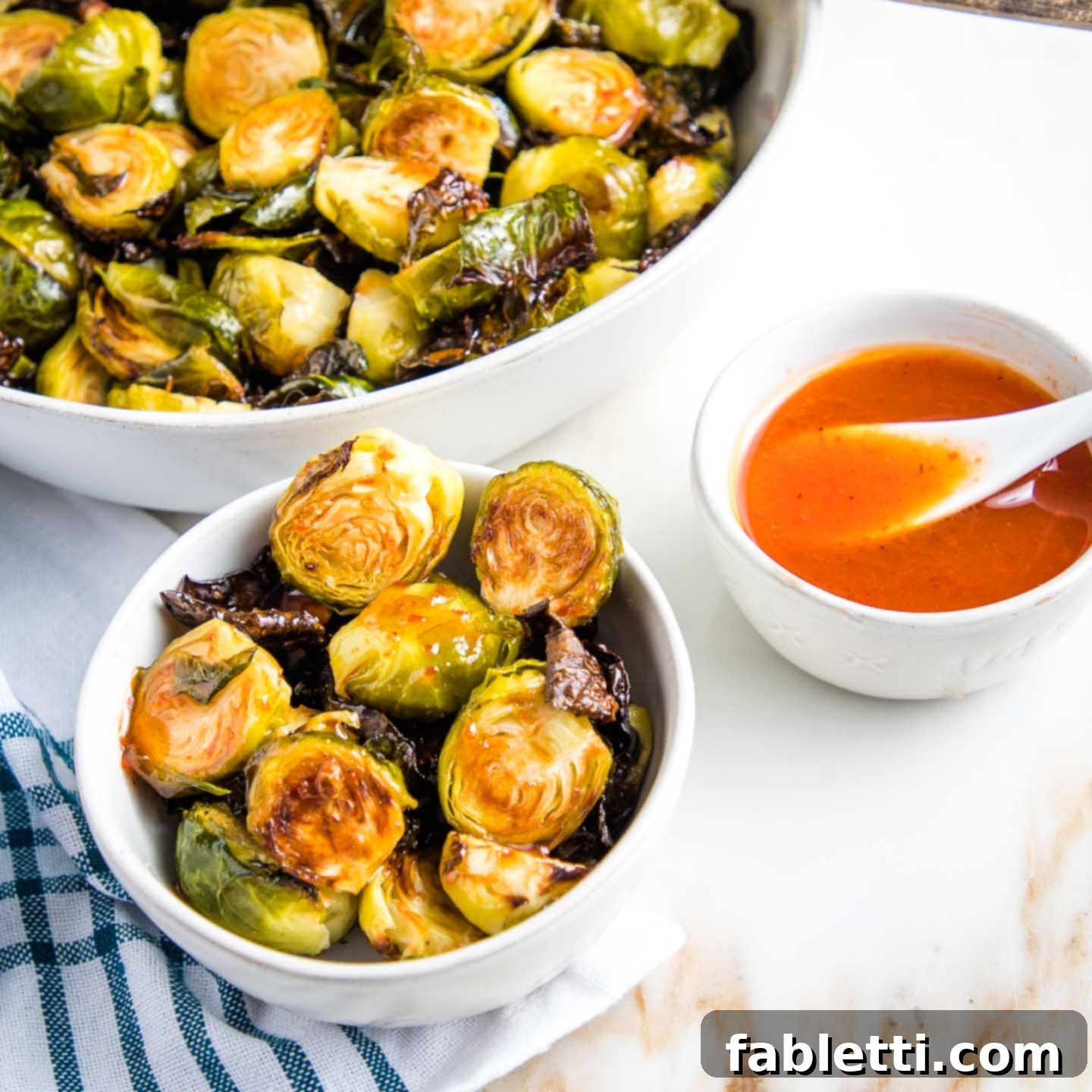 Honey Sriracha Glazed Crispy Roasted Brussels Sprouts 2 A beautifully arranged serving bowl of crispy brussels sprouts, with a separate small bowl showcasing sprouts drizzled generously with the gleaming honey-lime-sriracha sauce. An additional small bowl holds extra sauce, ready for dipping or adding more flavor.