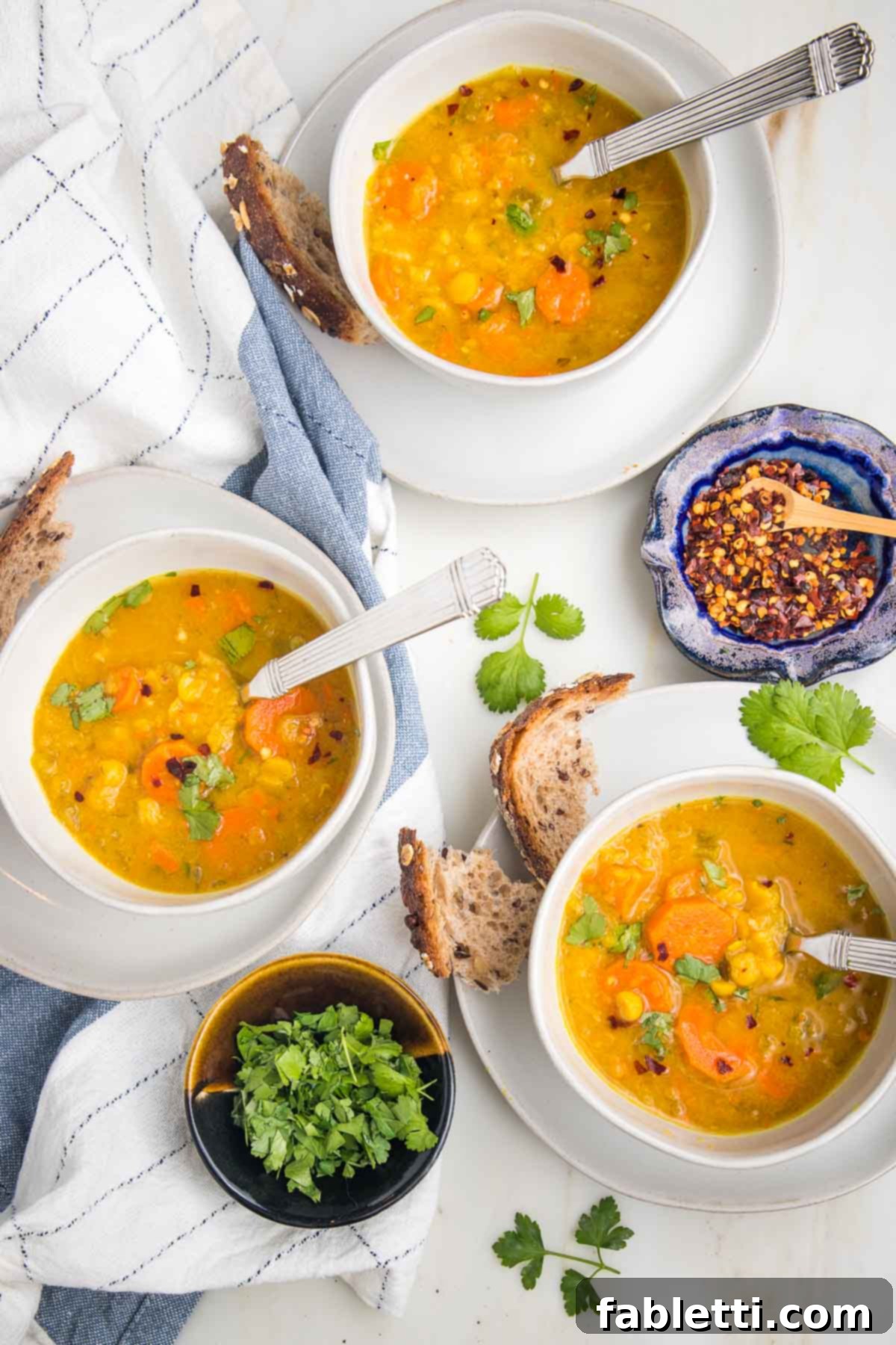 Hearty Vegan Yellow Split Pea Soup 2 Bowls of golden yellow split pea soup, garnished with fresh parsley and a sprinkle of crushed red pepper, served alongside crusty bread chunks on a rustic tea towel.