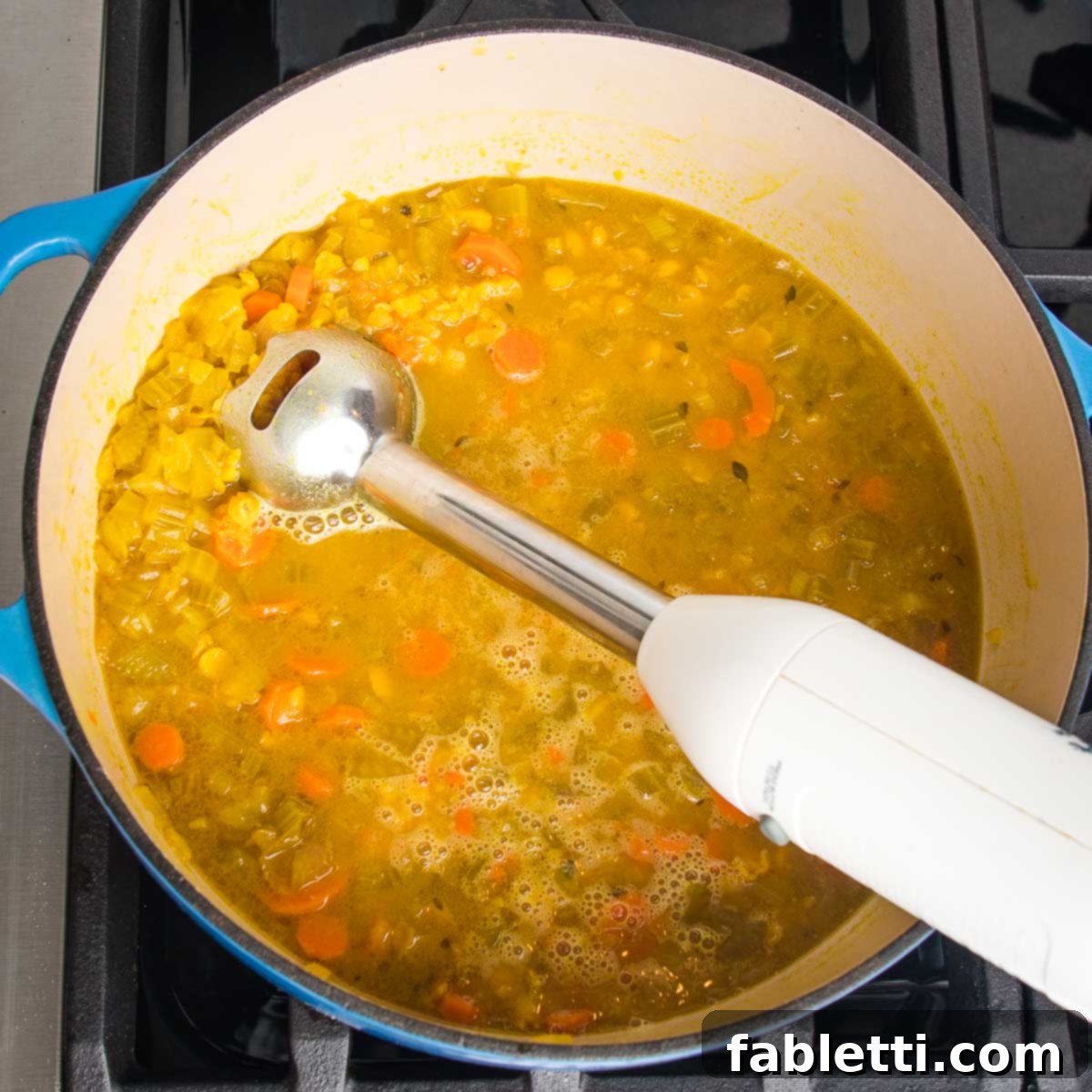 Hearty Vegan Yellow Split Pea Soup 12 A Dutch oven filled with chunky split pea soup, with an immersion blender partially submerged, ready for blending.