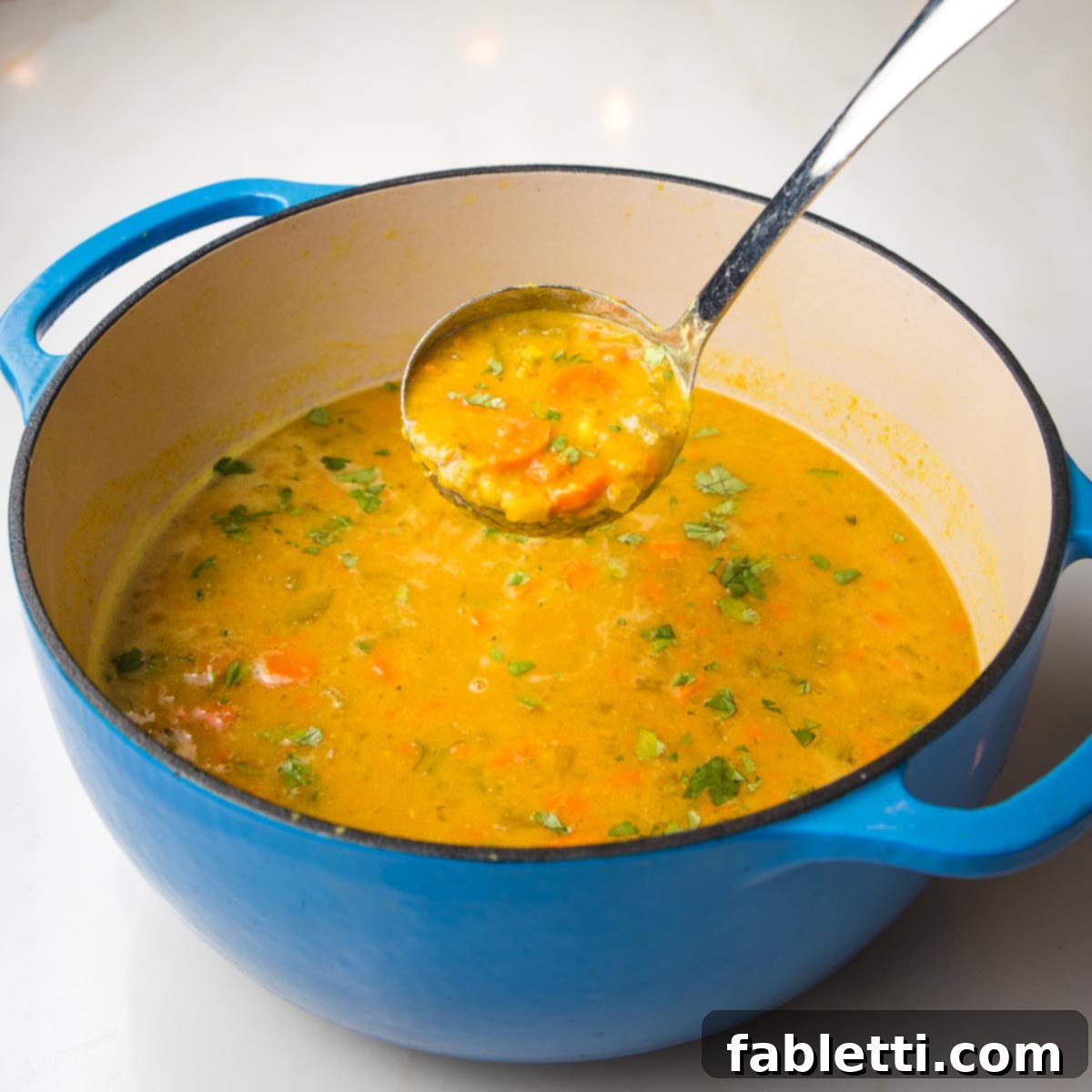 Hearty Vegan Yellow Split Pea Soup 13 A Dutch oven brimming with golden yellow split pea soup. A close-up shot reveals a ladleful of the soup, showcasing tender carrot pieces, creamy pureed peas, and vibrant fresh green herbs.