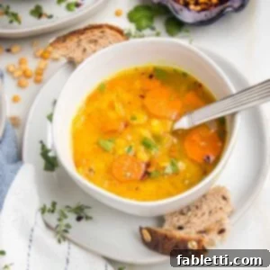 Hearty Vegan Yellow Split Pea Soup 15 White bowl filled with yellow split pea soup with carrots and fresh herbs. Crusty bread pieces on the plate holding the soup bowl.