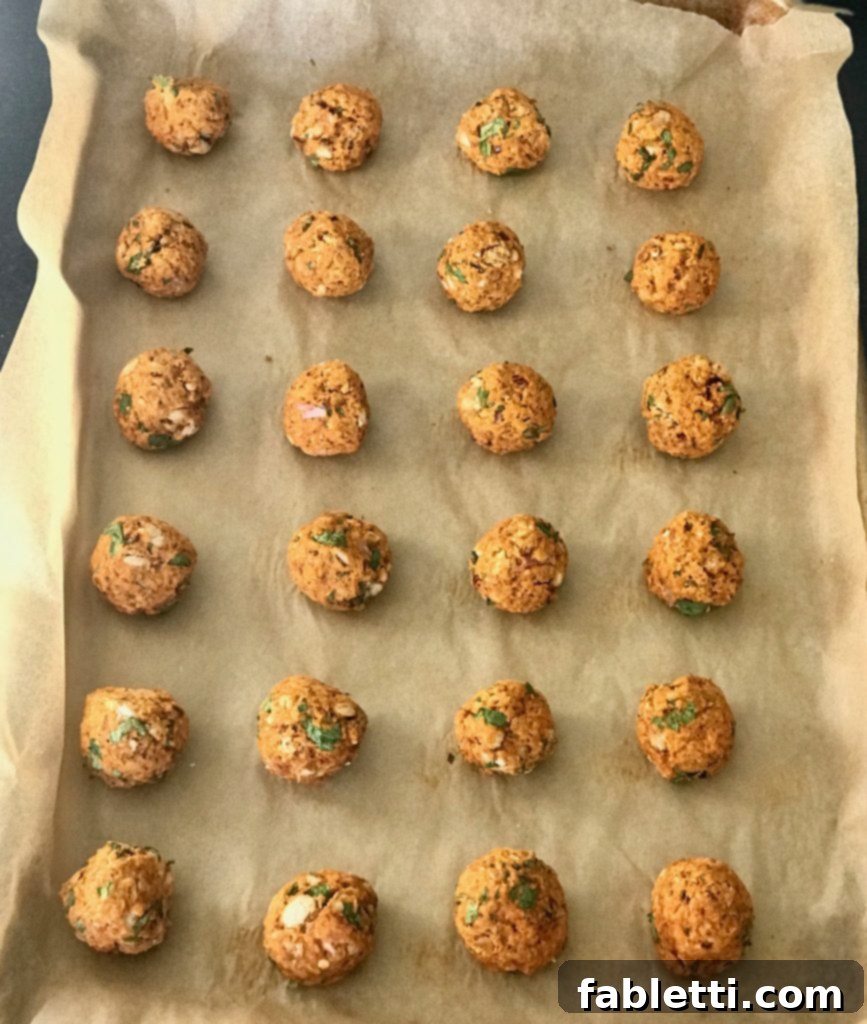 Neatly arranged rows of uncooked vegan meatballs resting on a parchment-lined baking tray, poised for their transformation in the oven.