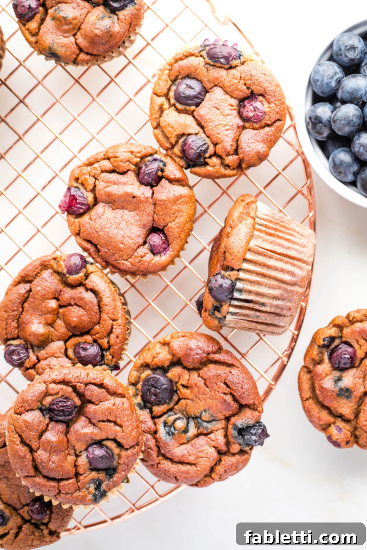 Quick Blender Almond Blueberry Muffins 2 Delicious almond flour blueberry muffins cooling on a rack, with fresh blueberries scattered nearby.
