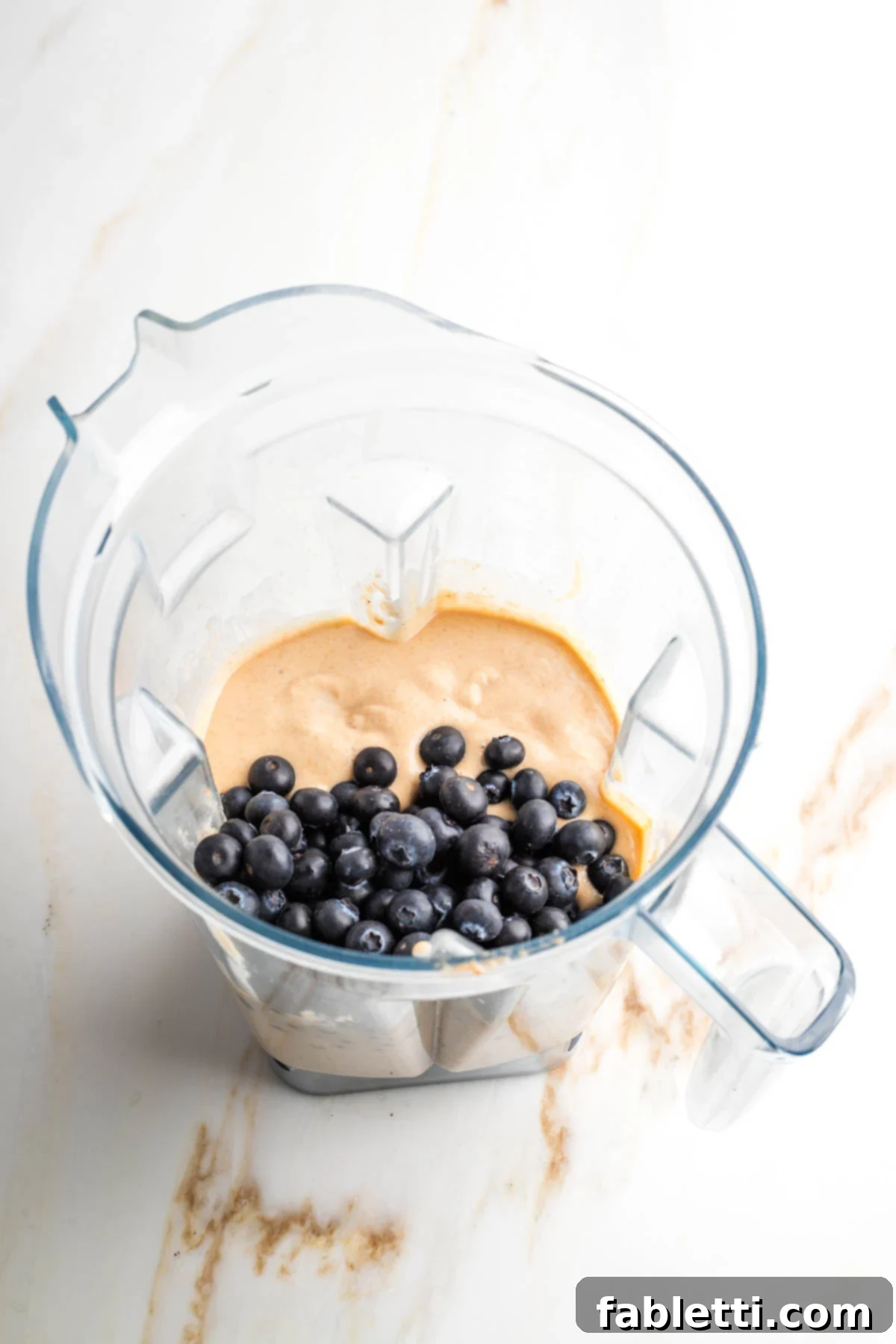 Quick Blender Almond Blueberry Muffins 6 Fresh blueberries being gently stirred into the smooth muffin batter in a blender pitcher.
