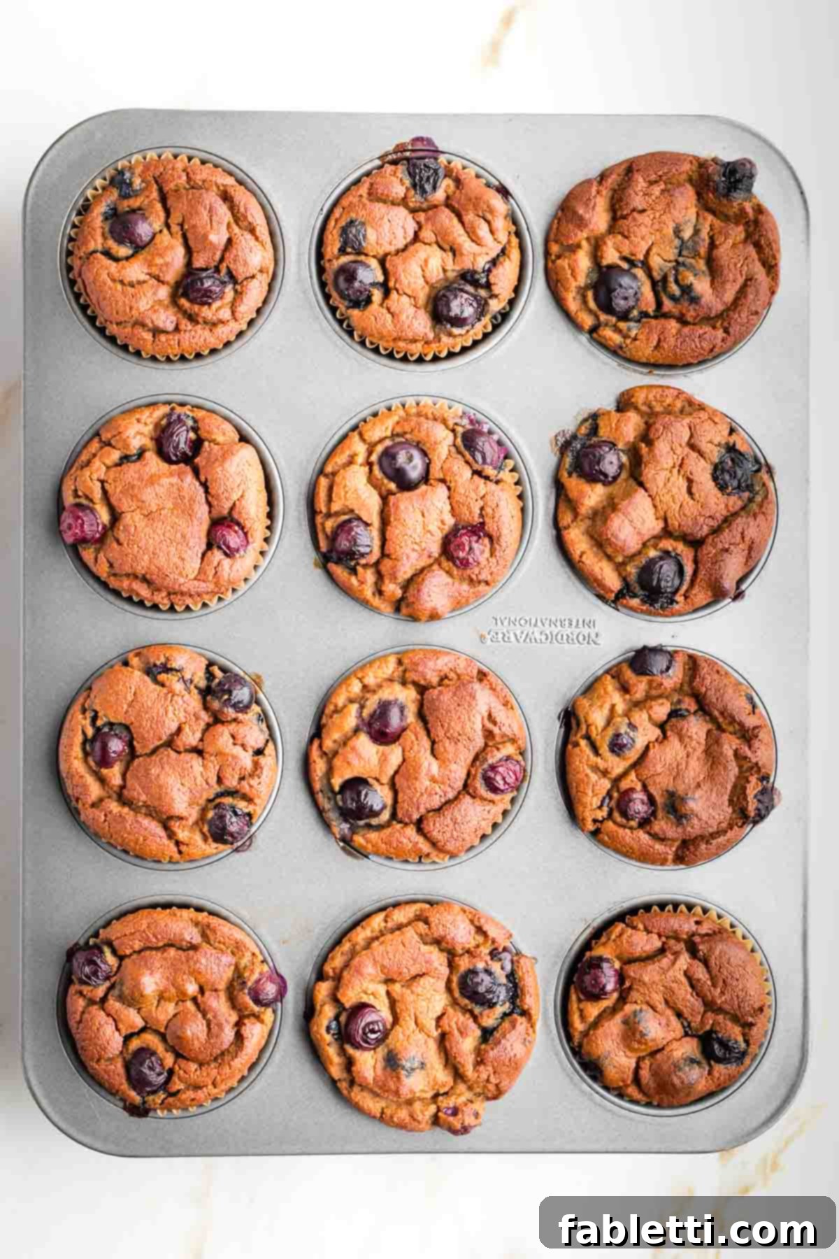 Quick Blender Almond Blueberry Muffins 8 A muffin tin filled with golden-brown blueberry muffins fresh from the oven.