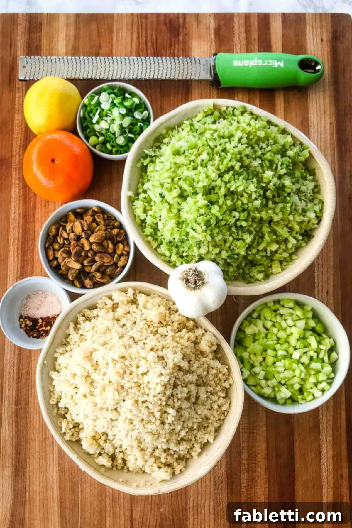 A vibrant flat lay of ingredients for riced broccoli and quinoa salad, featuring an orange, a lemon, chopped celery, pistachios, and seasonings like salt and pepper, ready for preparation.
