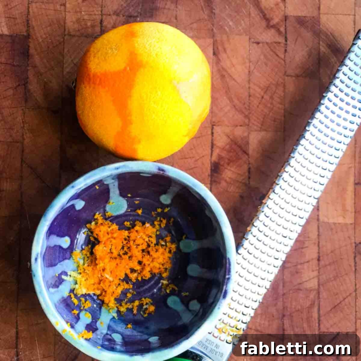 An orange being zested into a small white bowl with a microplane, preparing the base for the vibrant dressing.