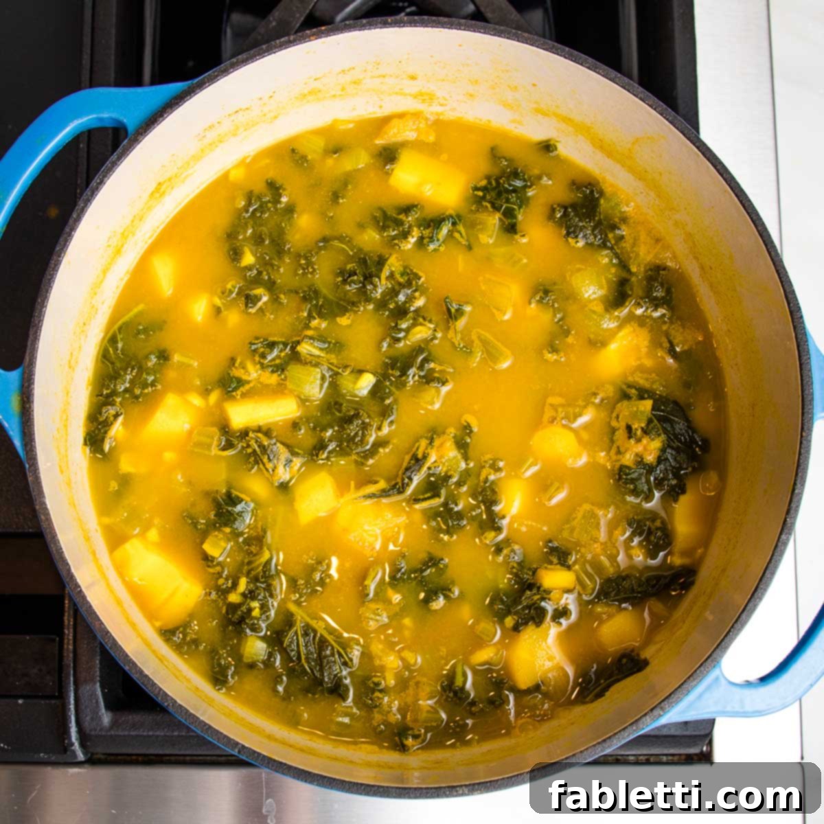 Nourishing Parsnip and Kale Soup 15 Dutch oven on the stovetop, filled with cooked kale and parsnips in a rich orange broth, ready to be blended.