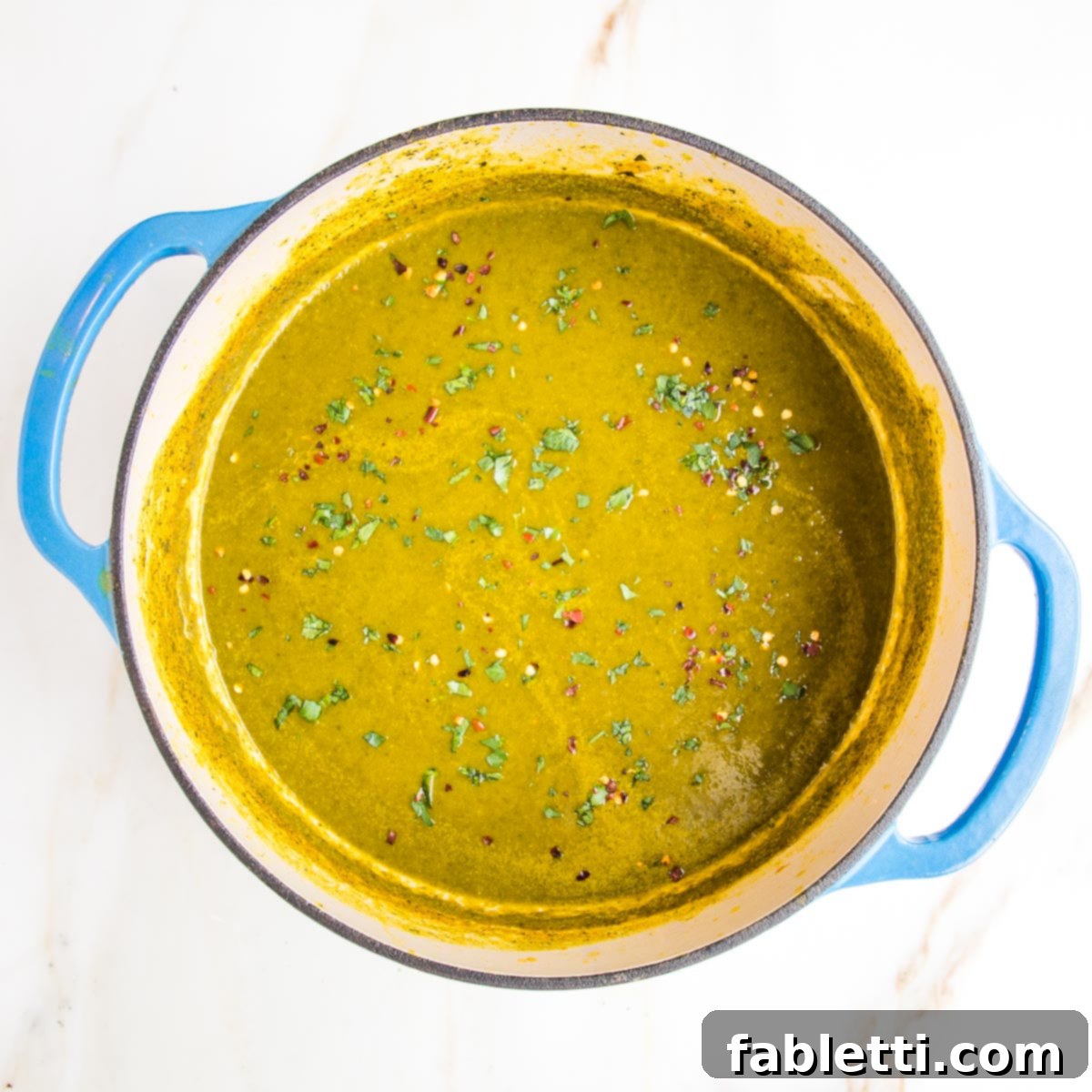 Nourishing Parsnip and Kale Soup 18 Blue Dutch oven filled with creamy kale soup, garnished with red pepper flakes, ready to serve.