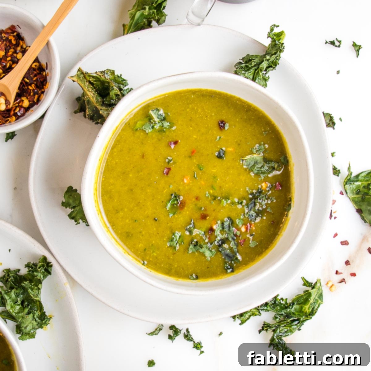 Nourishing Parsnip and Kale Soup 21 Parsnip and kale pureed soup in a white bowl, sprinkled with fresh herbs, crushed kale chips, and red pepper flakes, showcasing a beautiful garnish.
