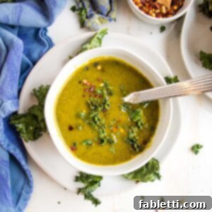 Nourishing Parsnip and Kale Soup 22 White bowl filled with green pureed soup that's sprinkled with kale chips and crushed red pepper flakes. Bowl is on top of a white saucer filled with more kale chips.
