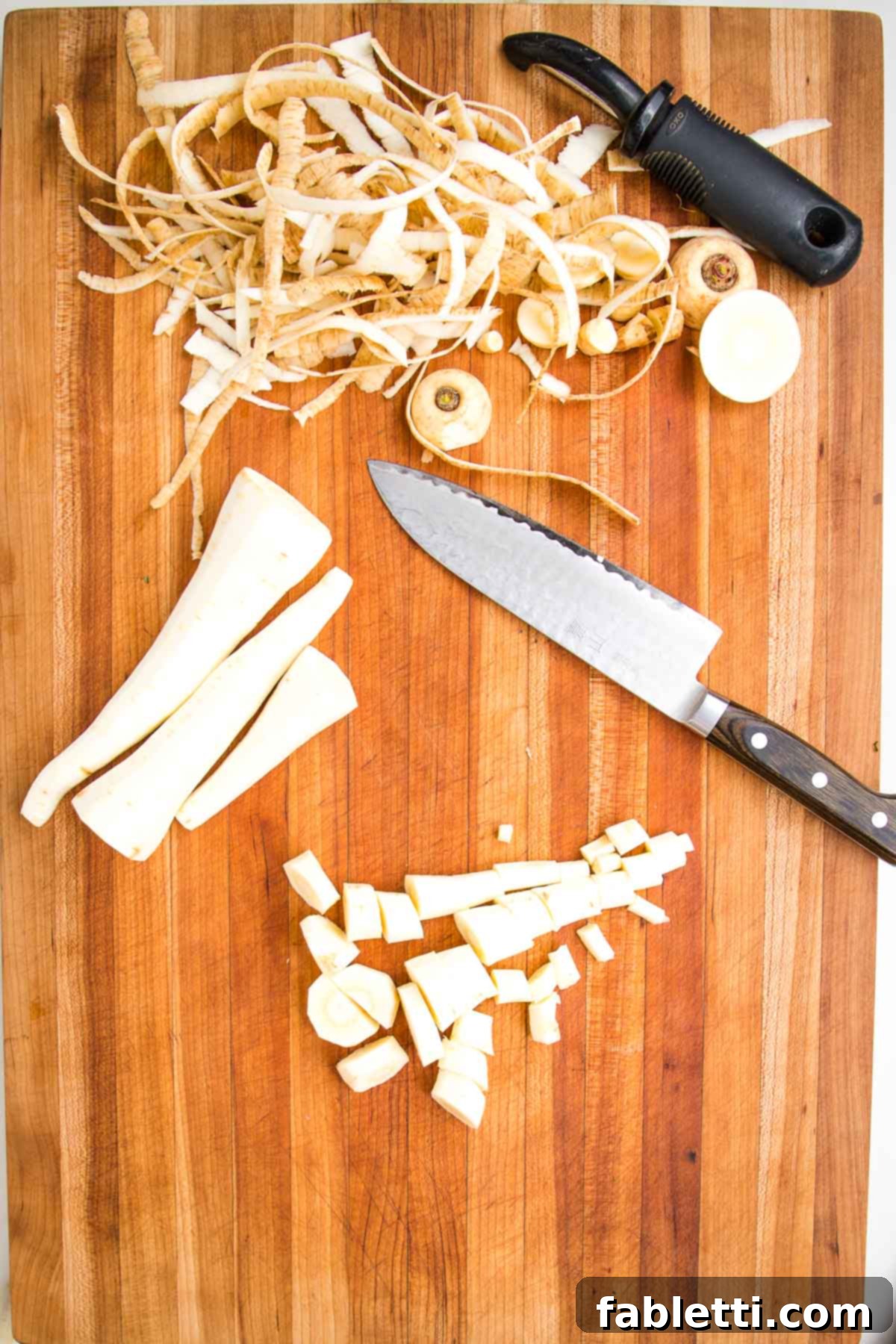 Nourishing Parsnip and Kale Soup 6 Wooden board with parsnip peels, a vegetable peeler, three peeled parsnips, and some chopped parsnips plus a chef's knife.