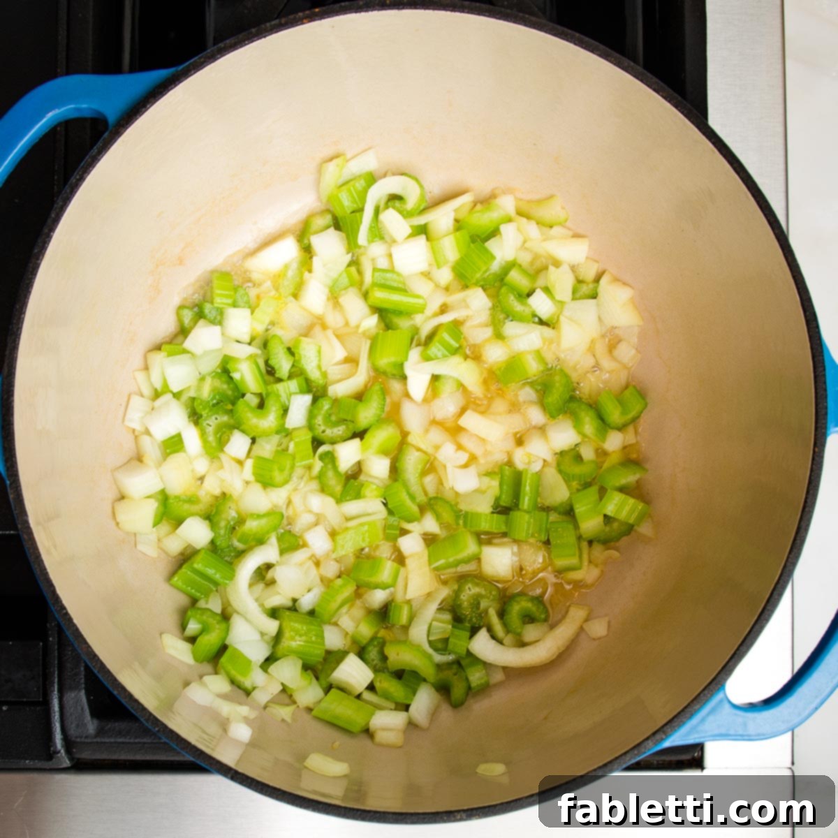 Nourishing Parsnip and Kale Soup 9 Close-up of onions and celery sautéing in a Dutch oven on the stovetop.