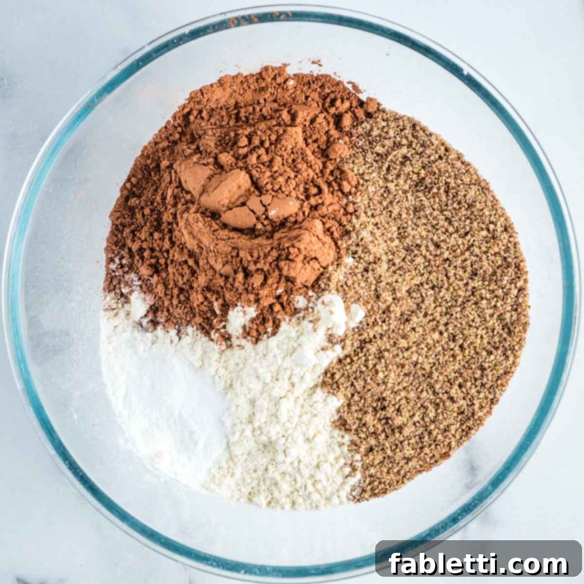 Decadent Vegan Double Chocolate Flax Muffins 4 Dry ingredients for muffins: flour, ground flax, cacao powder, baking powder, baking soda, and salt measured into a glass mixing bowl.