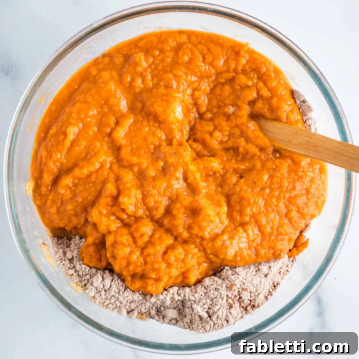 Decadent Vegan Double Chocolate Flax Muffins 7 Chocolate powdery dry ingredients with pumpkin puree mixture being poured into a glass mixing bowl.