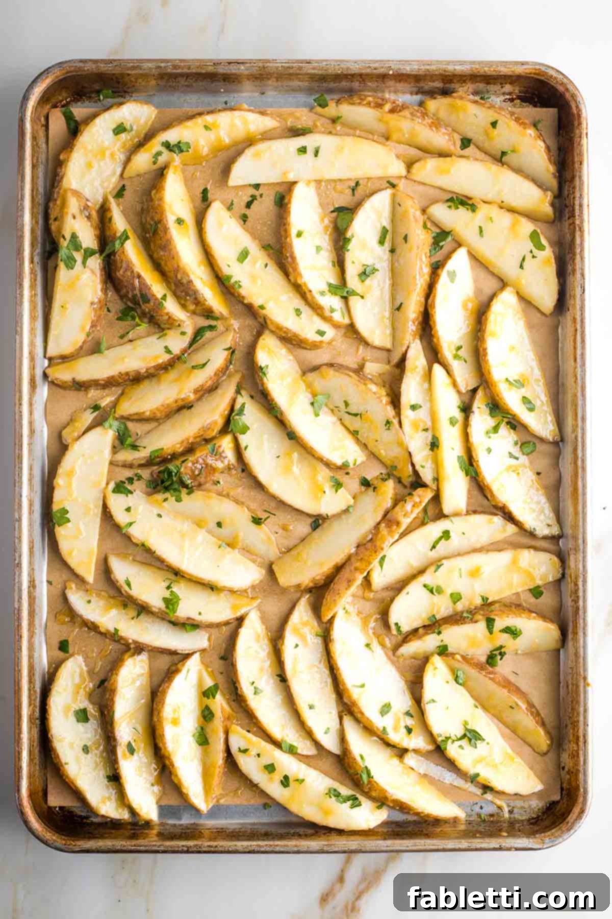 Golden Miso Crunch Potatoes 13 Potato wedges with miso marinade and parsley in a single layer on a baking tray.