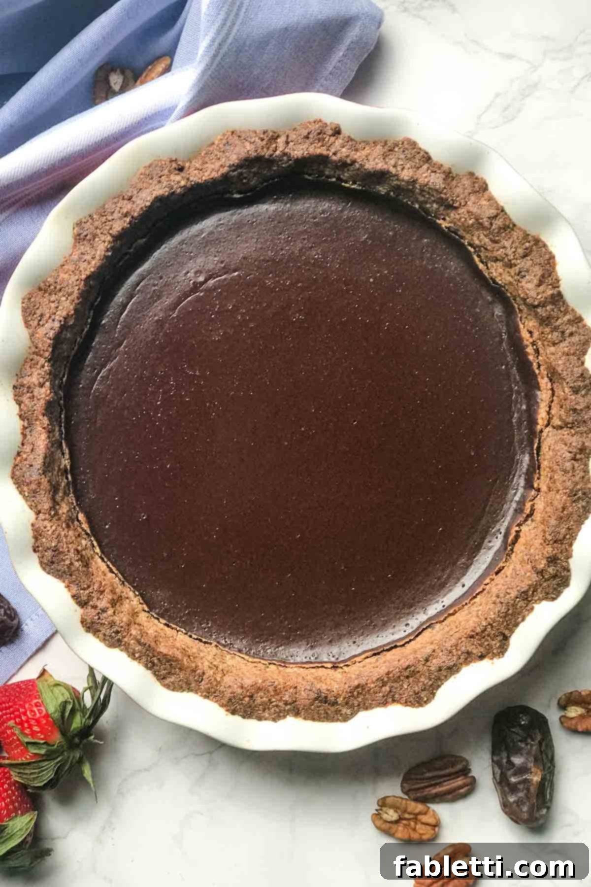 Guilt-Free Chocolate Pudding Pie 2 A slice of healthy chocolate pie with a creamy chocolate pudding filling set in a nutty crust, surrounded by fresh dates, pecans, and strawberries.