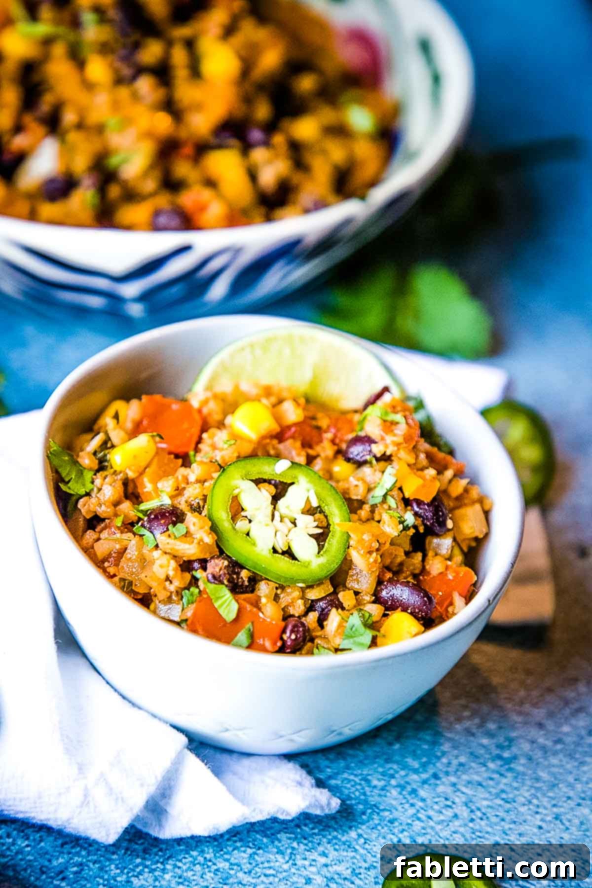 Flavorful Low Carb Mexican Cauliflower Rice 2 A vibrant bowl of Mexican cauliflower rice, garnished with fresh black beans, golden corn kernels, diced tomatoes, and slices of green jalapeño.
