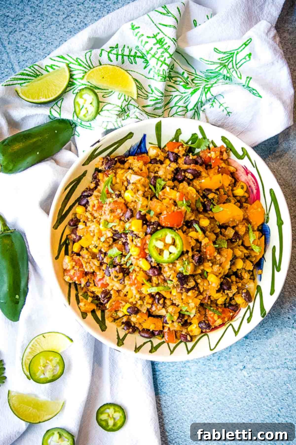 Flavorful Low Carb Mexican Cauliflower Rice 3 A close-up of colorful Mexican cauliflower rice with vibrant chunks of tomato, black beans, corn, and bright green jalapeño slices, ready to be served.
