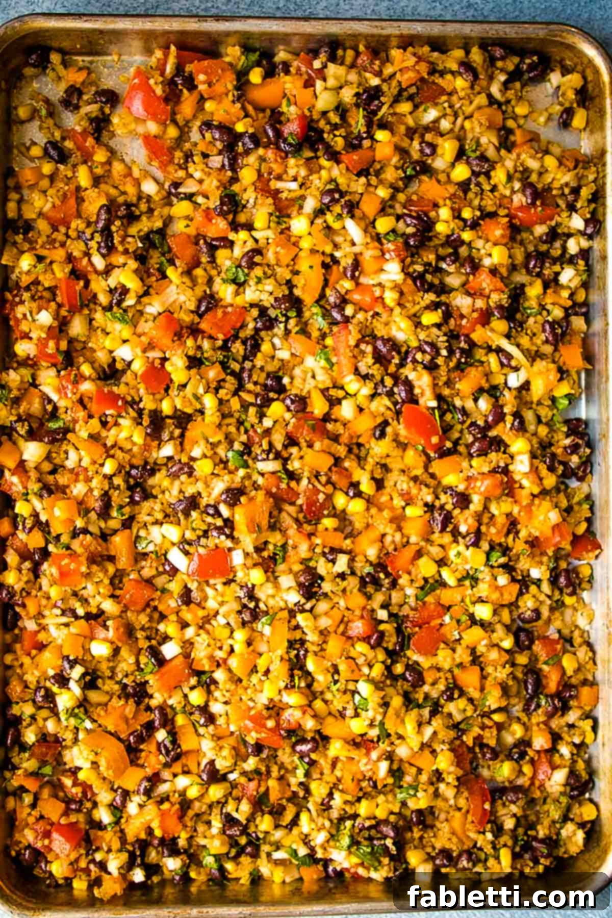 Flavorful Low Carb Mexican Cauliflower Rice 5 Mexican Cauliflower Rice on a sheet pan, seasoned with aromatic Mexican spices and mixed with diced tomatoes, vibrant bell peppers, black beans, sweet corn, and fresh cilantro, ready for roasting.