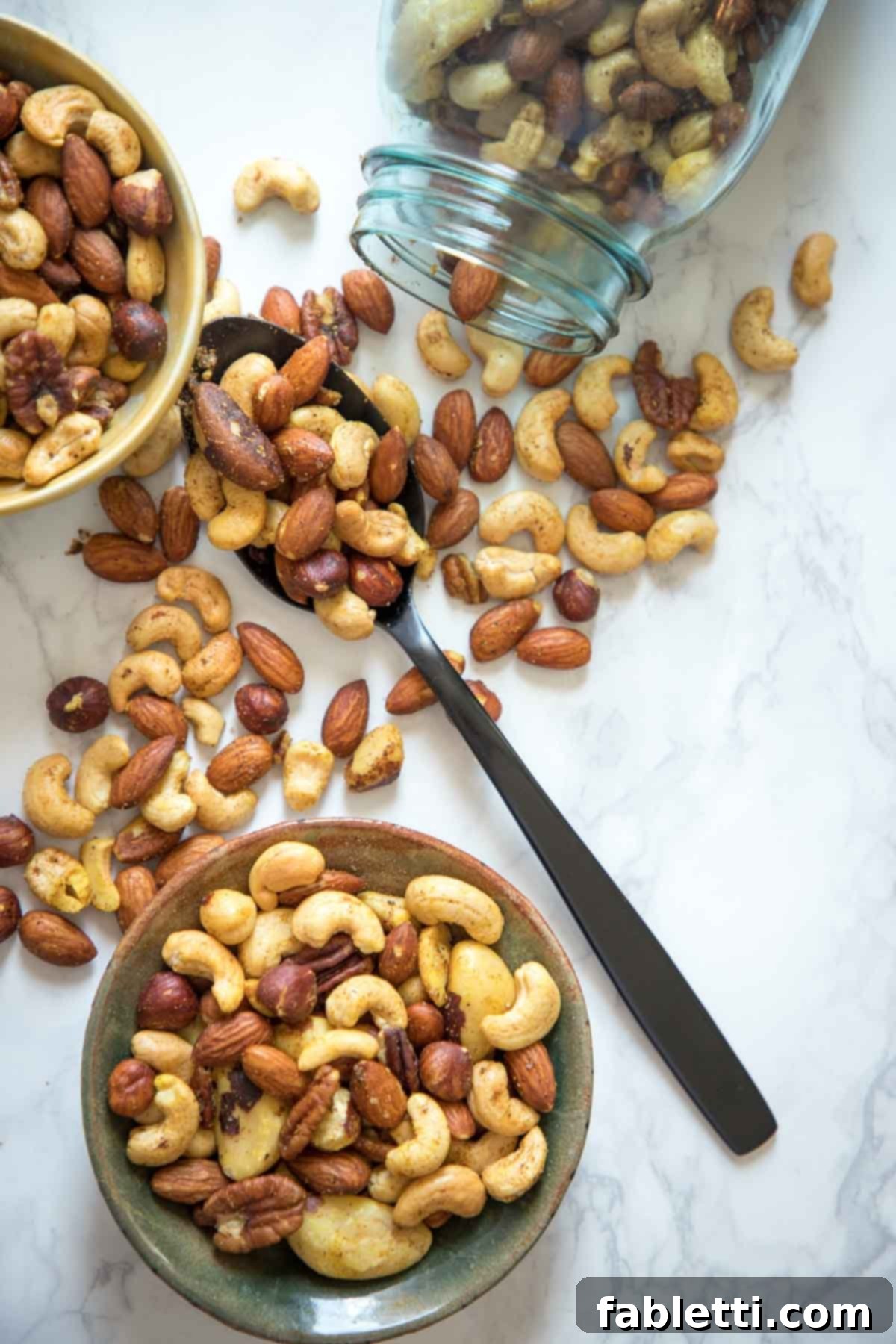 Spiced nuts spilling out of a jar and spooned into a bowl.
