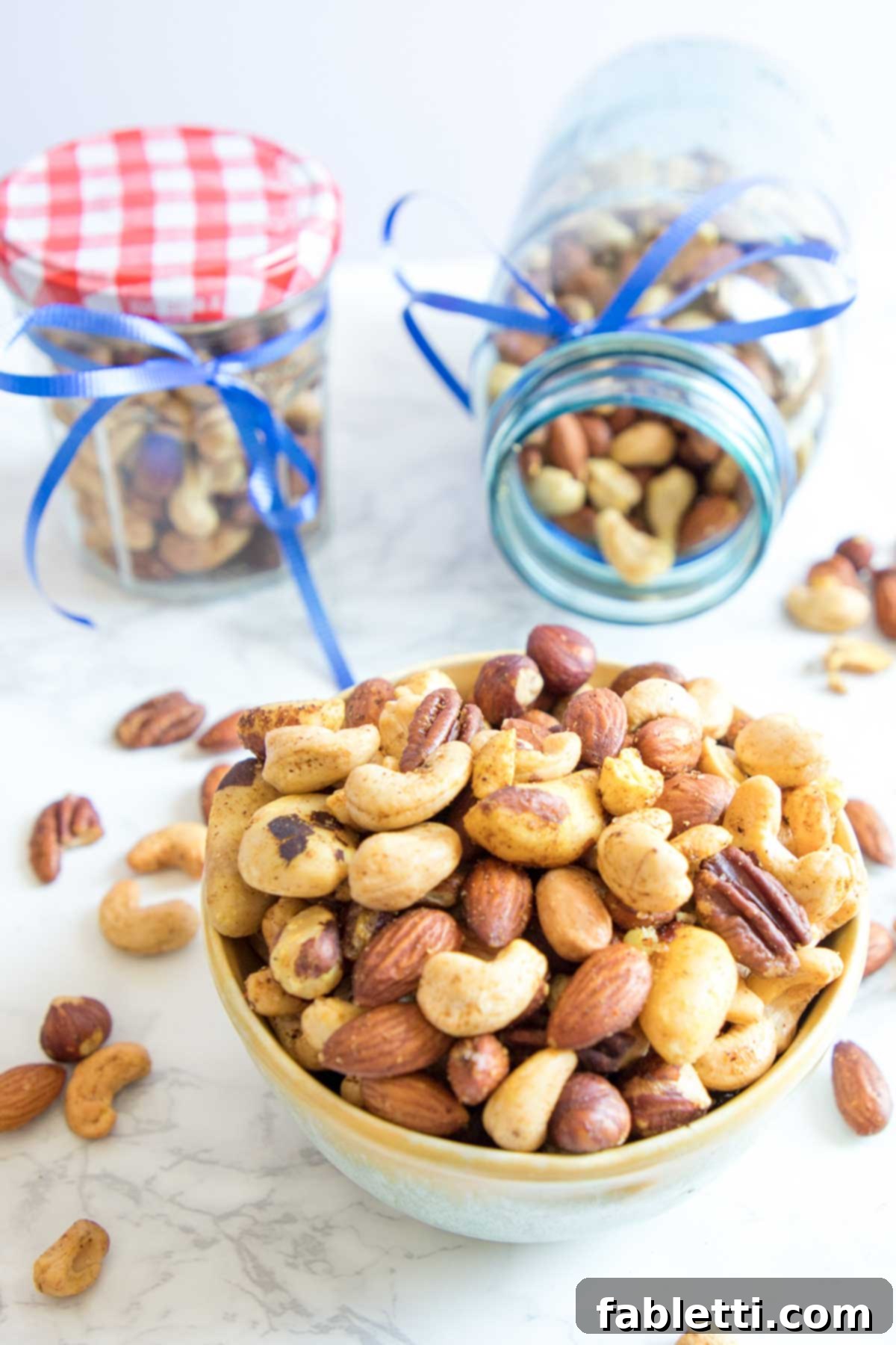 Festive jars of assorted nuts with spices spilling out and into a bowl.