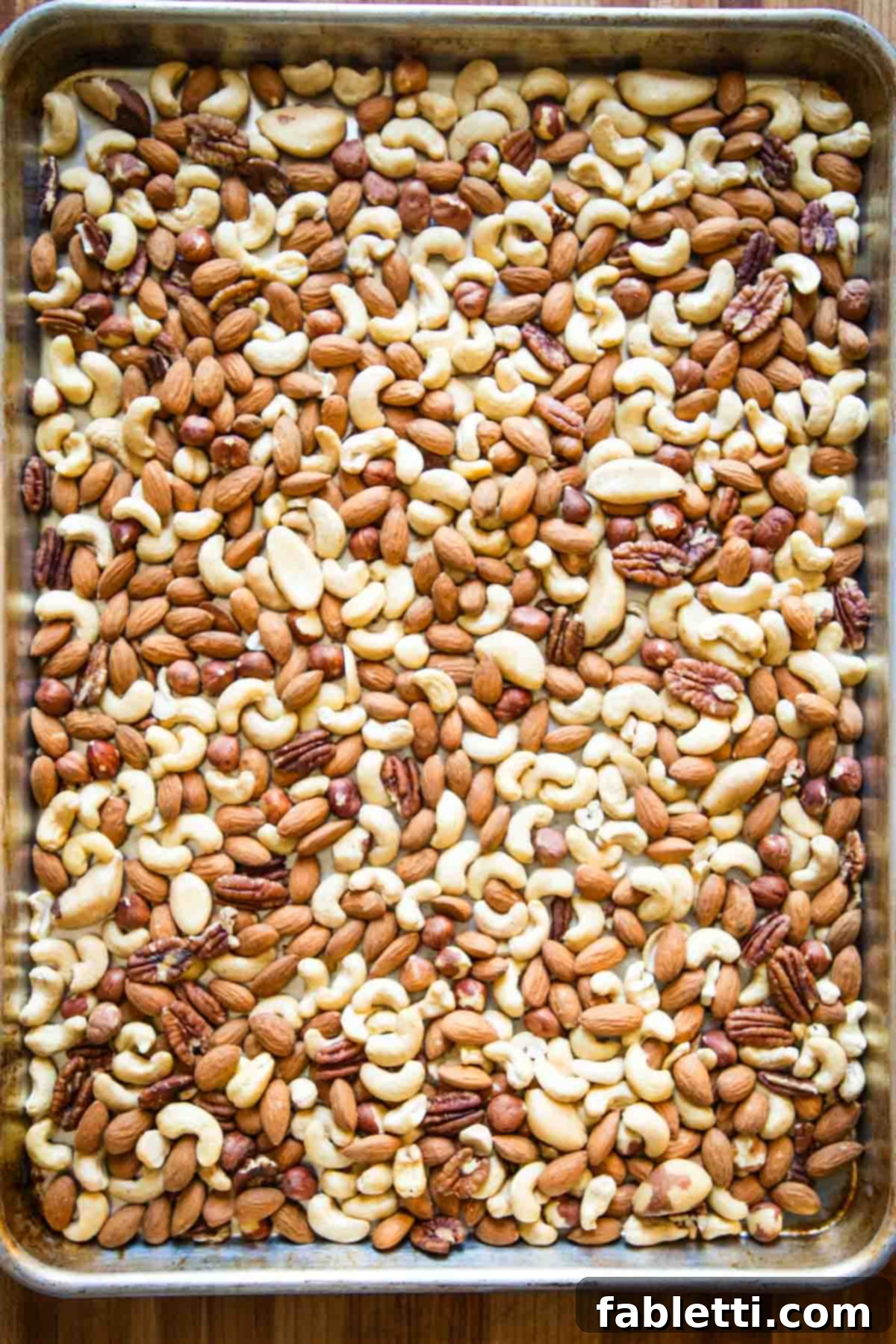Large rimmed baking tray with assorted nuts in a single layer.