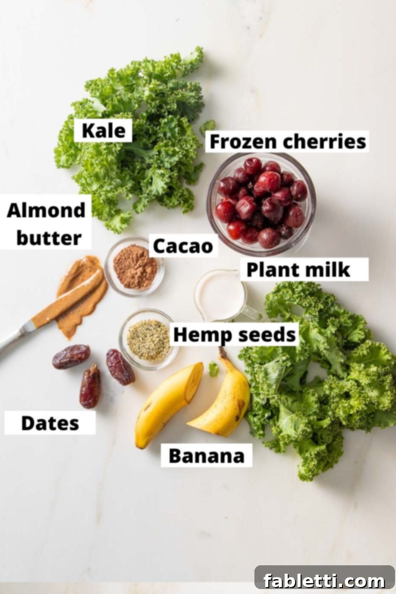 A top-down view of carefully arranged smoothie ingredients on a wooden surface, including fresh kale, a bowl of frozen cherries, a carton of plant milk, a banana, a small bowl of hemp seeds, pitted dates, a jar of almond butter, and a scoop of cacao powder. Each ingredient is clearly labeled.