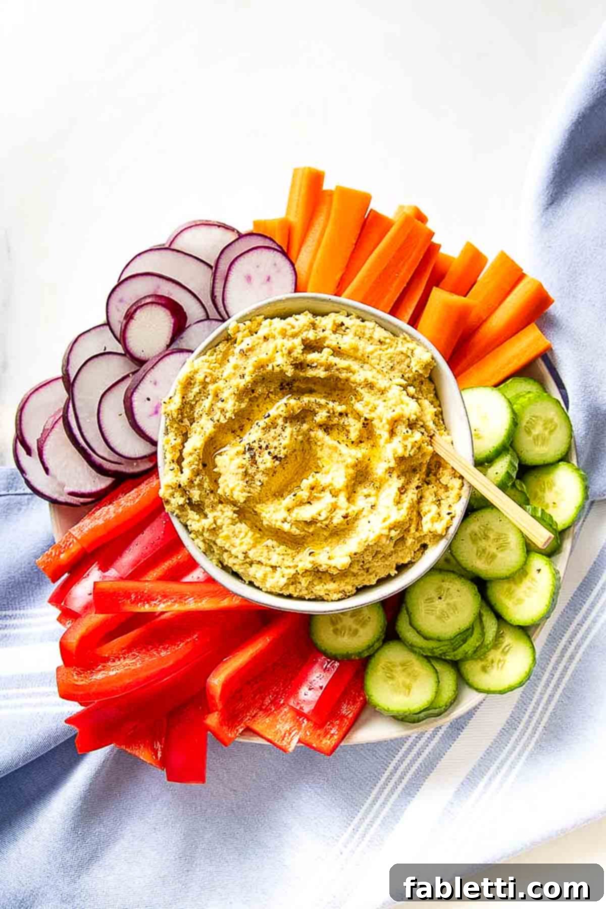 Smoky Roasted Cauliflower Hummus 2 Hummus in a bowl, surrounded by vibrant sliced veggies.