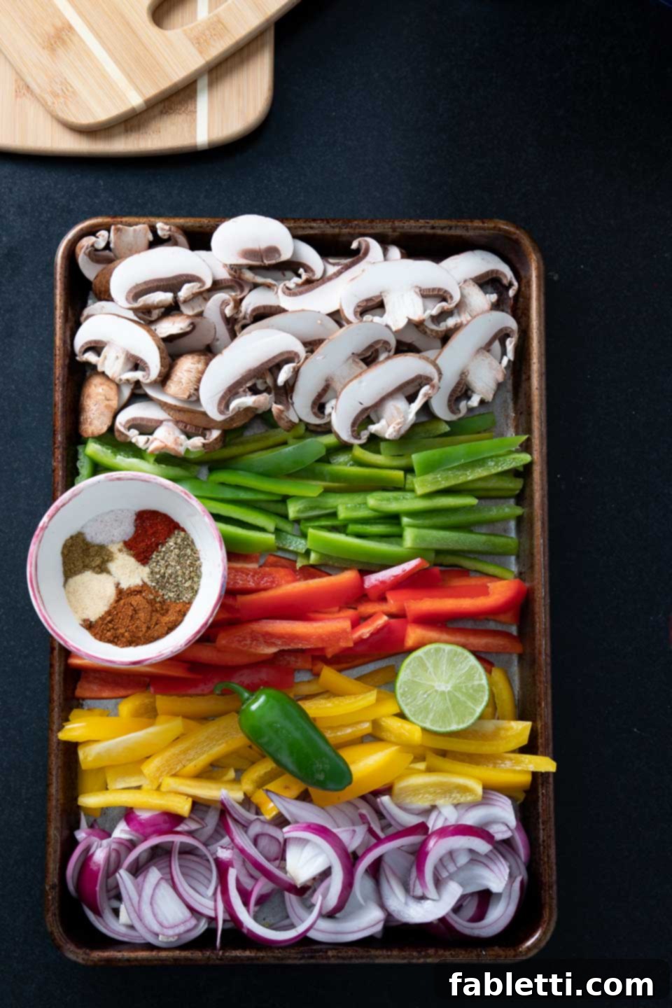 Colorful rows of sliced veggies on a sheet pan with a bowl of mexican spices. 