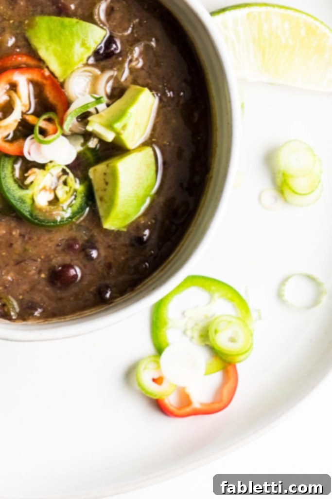 No-Fuss Black Bean Soup 11 A delicious bowl of black bean soup, generously topped with creamy avocado chunks, spicy sliced jalapenos, and fresh green scallions, enhancing both flavor and visual appeal.