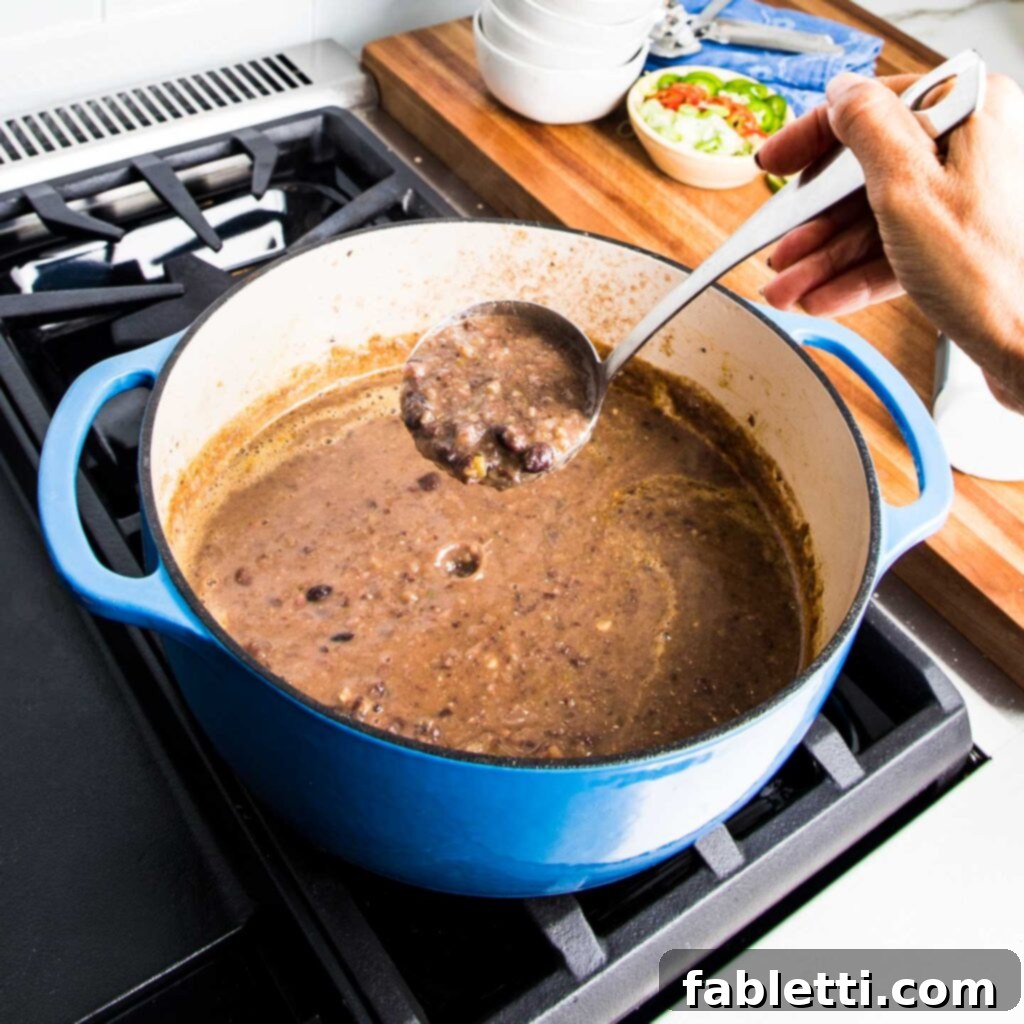 No-Fuss Black Bean Soup 10 A ladle lifts a portion of rich, pureed black bean soup from a vibrant blue Dutch oven, showcasing its smooth texture.