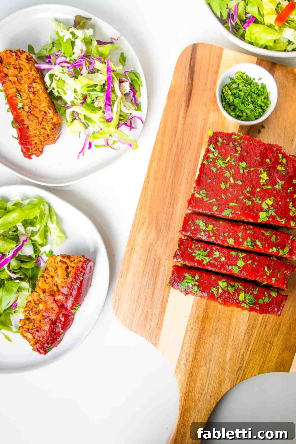 Hearty Plant-Based Meatloaf 2 Perfectly sliced vegan meatloaf on a cutting board, alongside plates with servings of meatloaf and a fresh side salad.