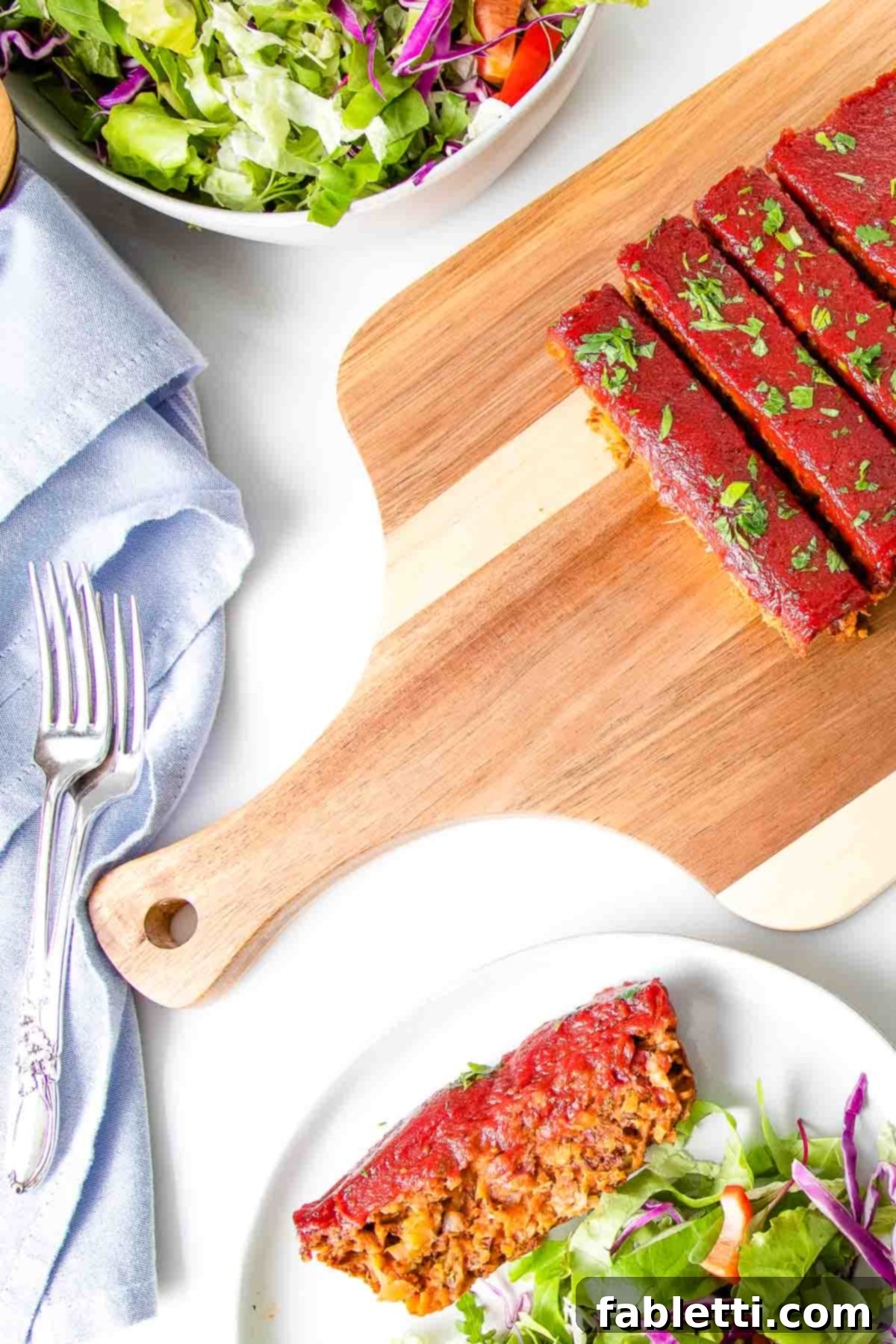 Hearty Plant-Based Meatloaf 17 Slices of vegan meatloaf with tomato glaze on a wooden cutting board, with a plate holding a serving of meatloaf and a side salad.