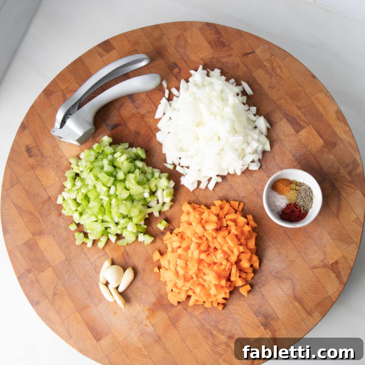Hearty Plant-Based Meatloaf 5 A round wooden board with neatly diced onions, celery, carrots, and minced garlic, accompanied by a small dish of measured spices.