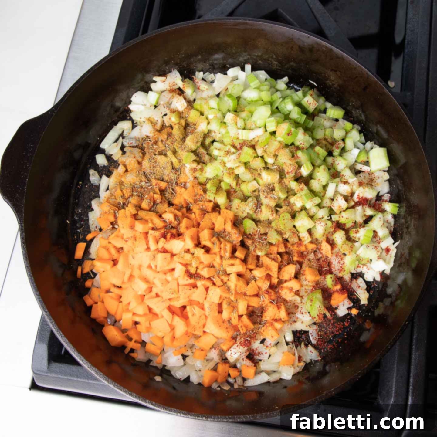 Hearty Plant-Based Meatloaf 6 A cast iron skillet containing sauteed diced vegetables, lightly sprinkled with spices, cooking on the stovetop.