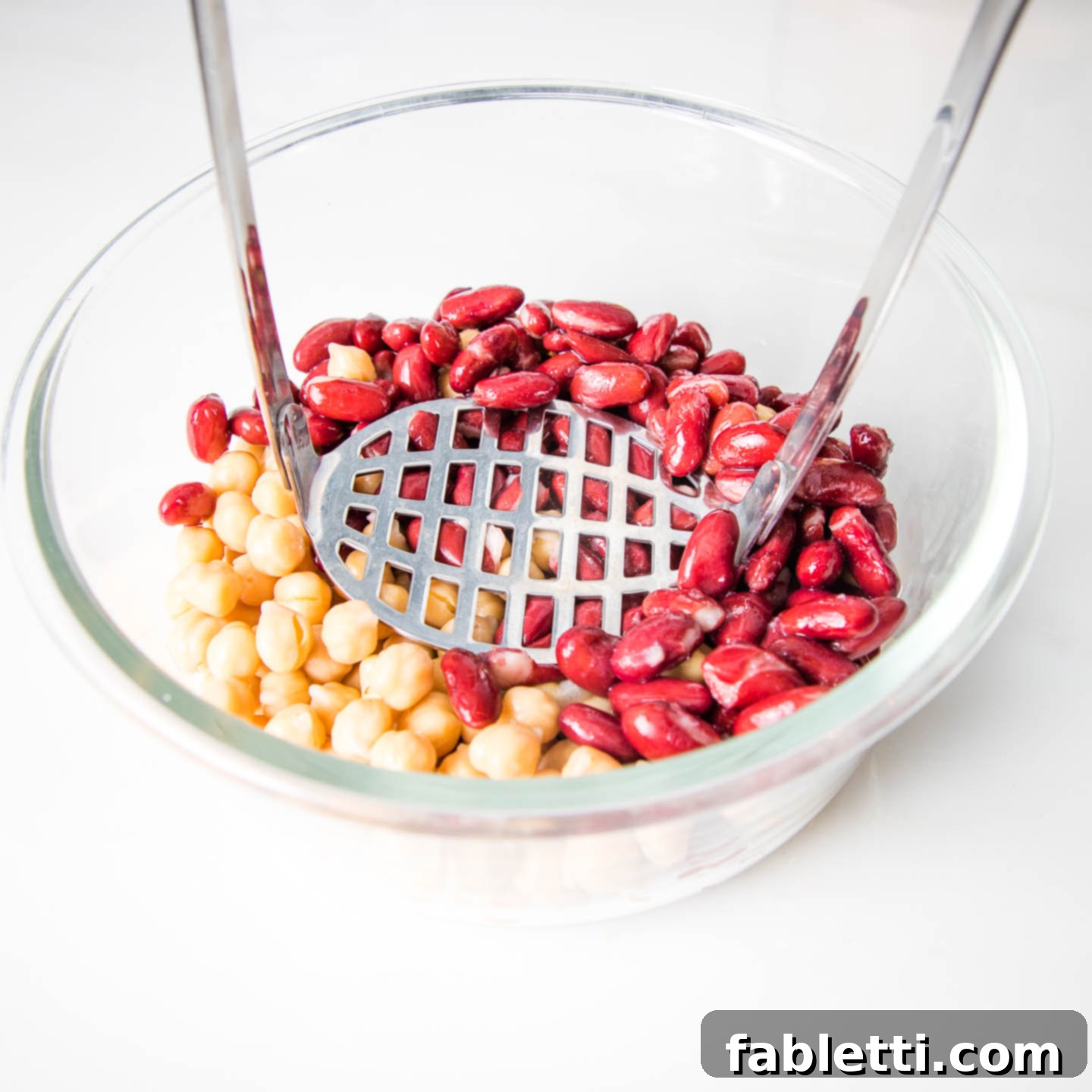 Hearty Plant-Based Meatloaf 7 A glass bowl containing two colors of beans (kidney and chickpeas) ready for mashing, with a masher nearby.