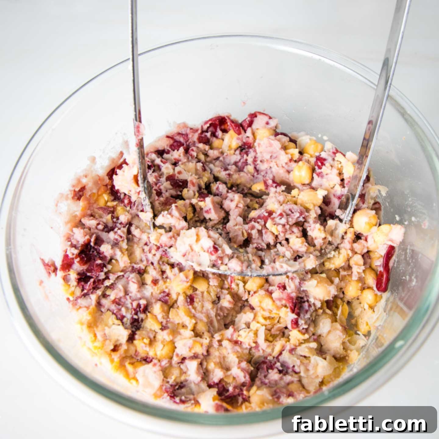 Hearty Plant-Based Meatloaf 8 Mashing beans with a potato masher in a large glass mixing bowl, creating a textured mixture.