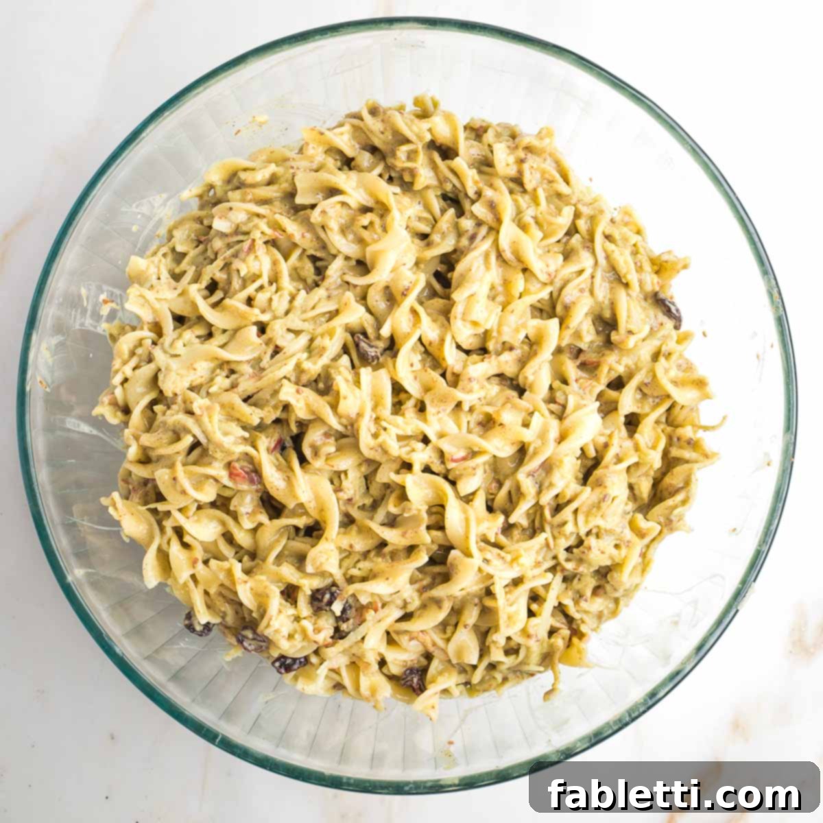 Delicious Dairy-Free Apple Noodle Kugel 11 A large glass mixing bowl holds the thoroughly combined noodle pudding mixture, showcasing its readiness for baking with all ingredients evenly coated.
