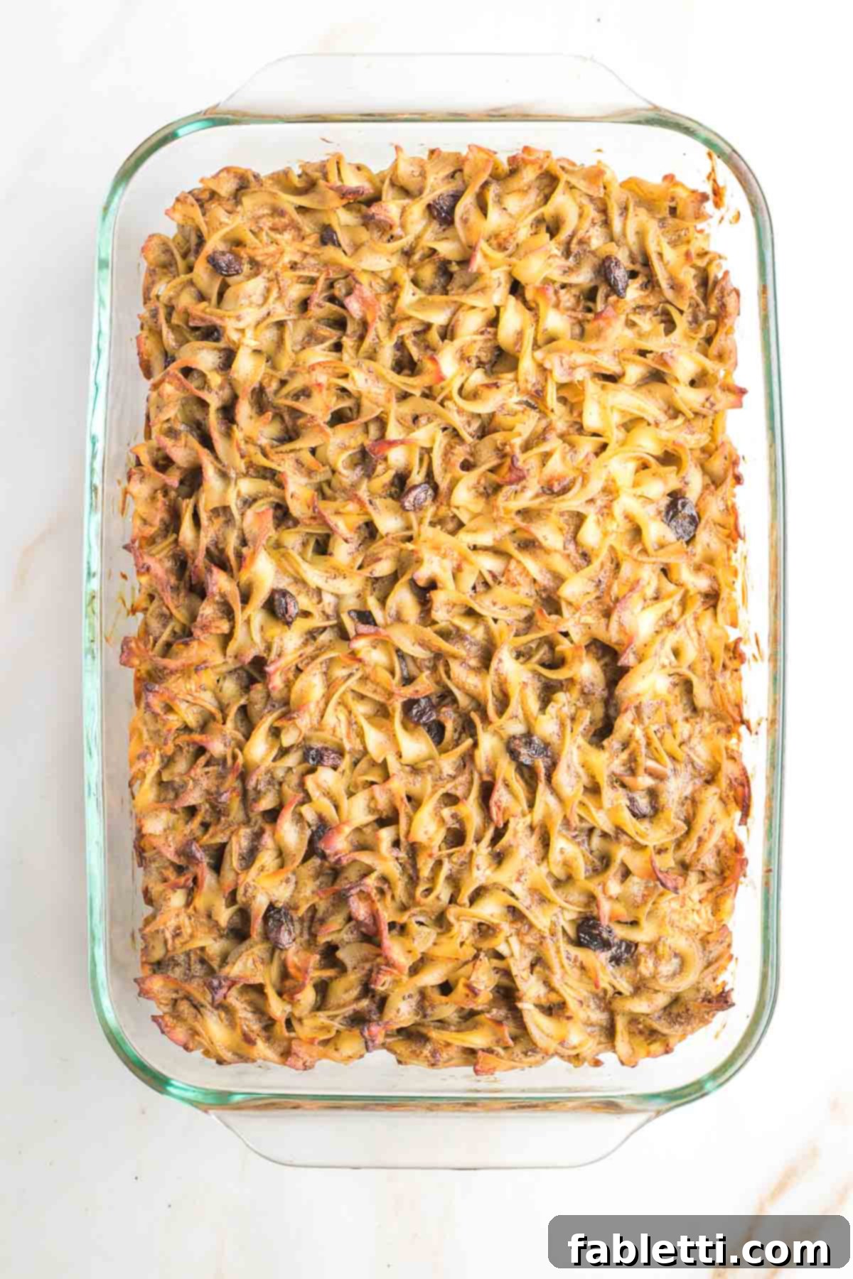 Delicious Dairy-Free Apple Noodle Kugel 13 The freshly baked apple raisin noodle kugel, golden brown and bubbling, is shown in a 9x13 casserole dish, highlighting its irresistible crunchy noodle top and ready-to-serve appearance.