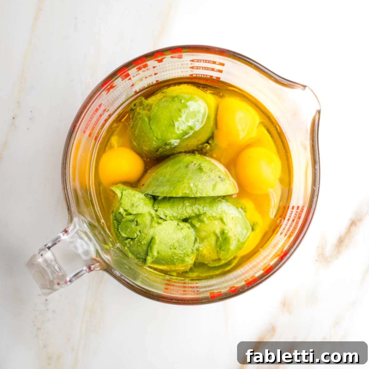 Delicious Dairy-Free Apple Noodle Kugel 4 Whole eggs, creamy avocado, golden olive oil, and sweet honey are precisely measured and added into a medium mixing bowl, forming the rich, dairy-free base for the apple noodle kugel.