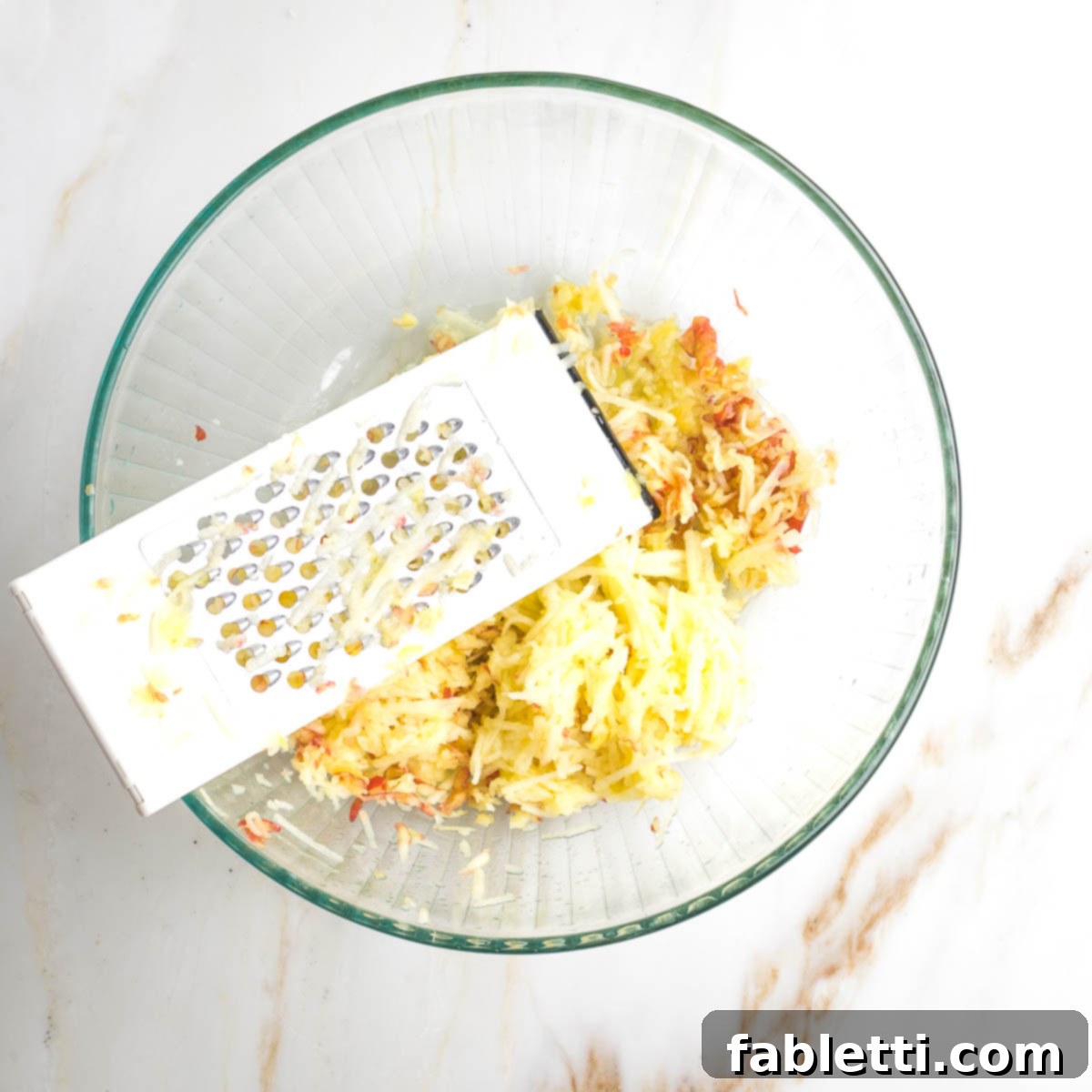 Delicious Dairy-Free Apple Noodle Kugel 8 Fresh apples are being skillfully shredded using the coarse side of a box grater directly into a large mixing bowl, creating the vibrant, fruity core of the kugel.