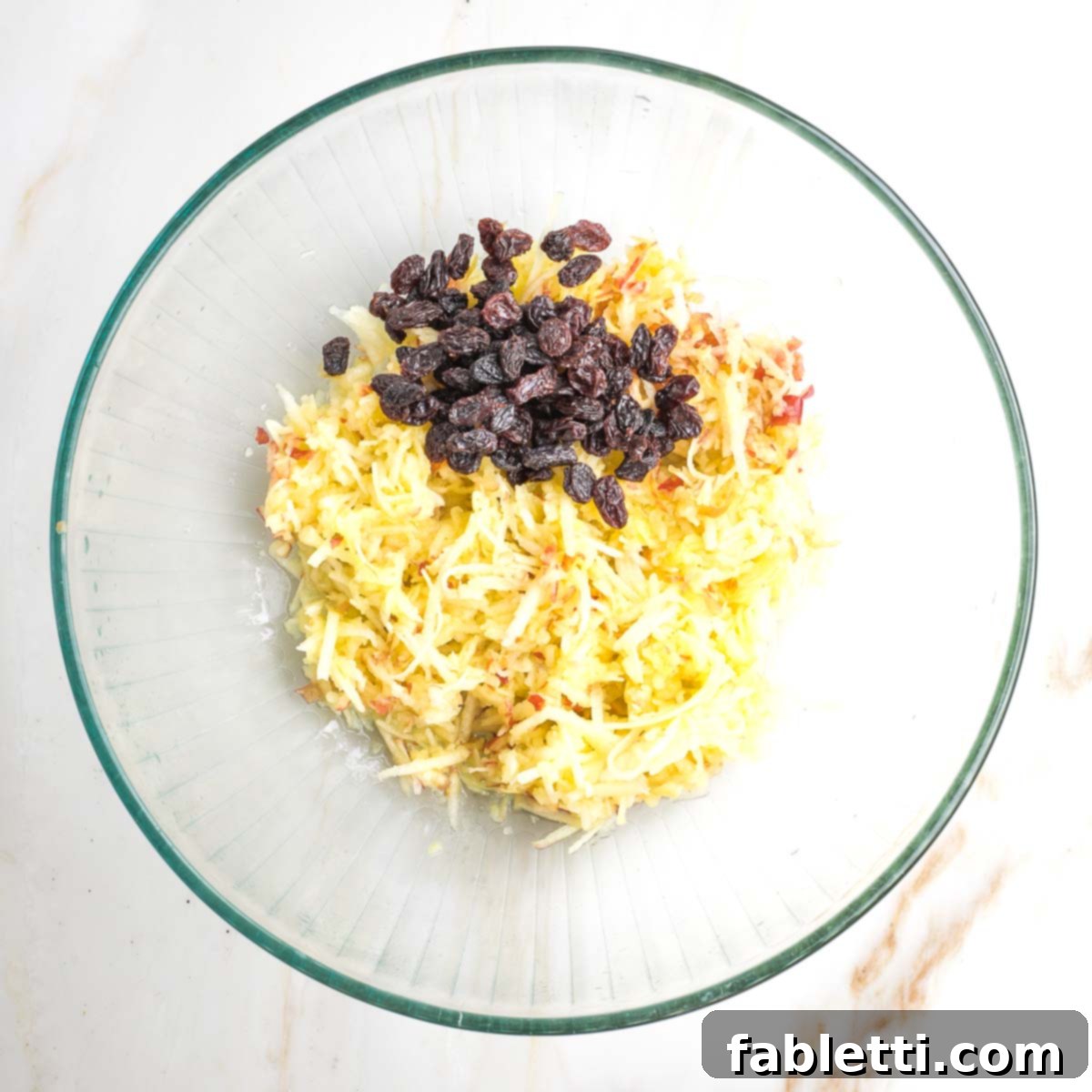 Delicious Dairy-Free Apple Noodle Kugel 9 A generous amount of dark raisins is added to the bowl containing the freshly shredded apples, creating a sweet and fruity combination for the kugel.