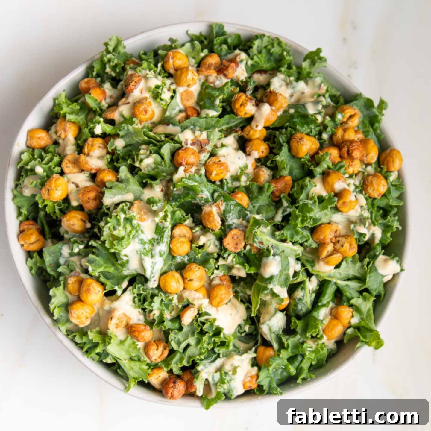 Large bowl filled with bright green massaged kale, creamy vegan Caesar dressing, and crispy roasted chickpeas