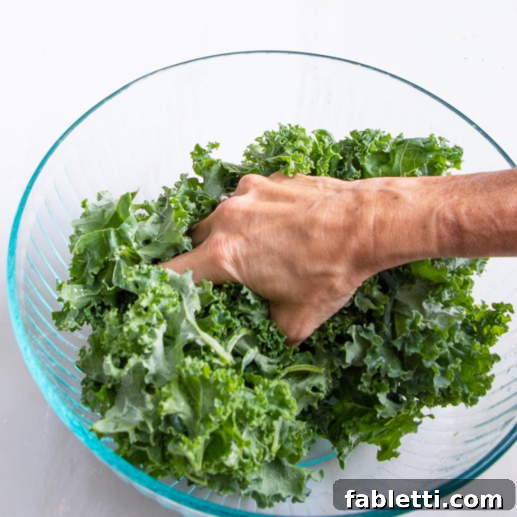Hands massaging kale in a bowl to soften its texture